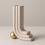 Cargar imagen en el visor de la Galería, Jarrón decorativo Oguz beige moderno en forma de L con base de esfera dorada sobre fondo beige.
