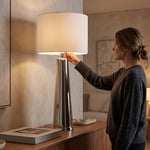 Cargar imagen en el visor de la Galería, Mujer encendiendo la lámpara de mesa metálica cromo oro 102 cm sobre un aparador de madera.