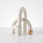 Cargar imagen en el visor de la Galería, Accesorio decorativo Farid blanco con arcos curvos y detalle de esfera dorada para mesa o estante.