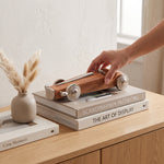 Cargar imagen en el visor de la Galería, Mano colocando la figura Carro Velluto de madera decorativa sobre libros en un mueble.