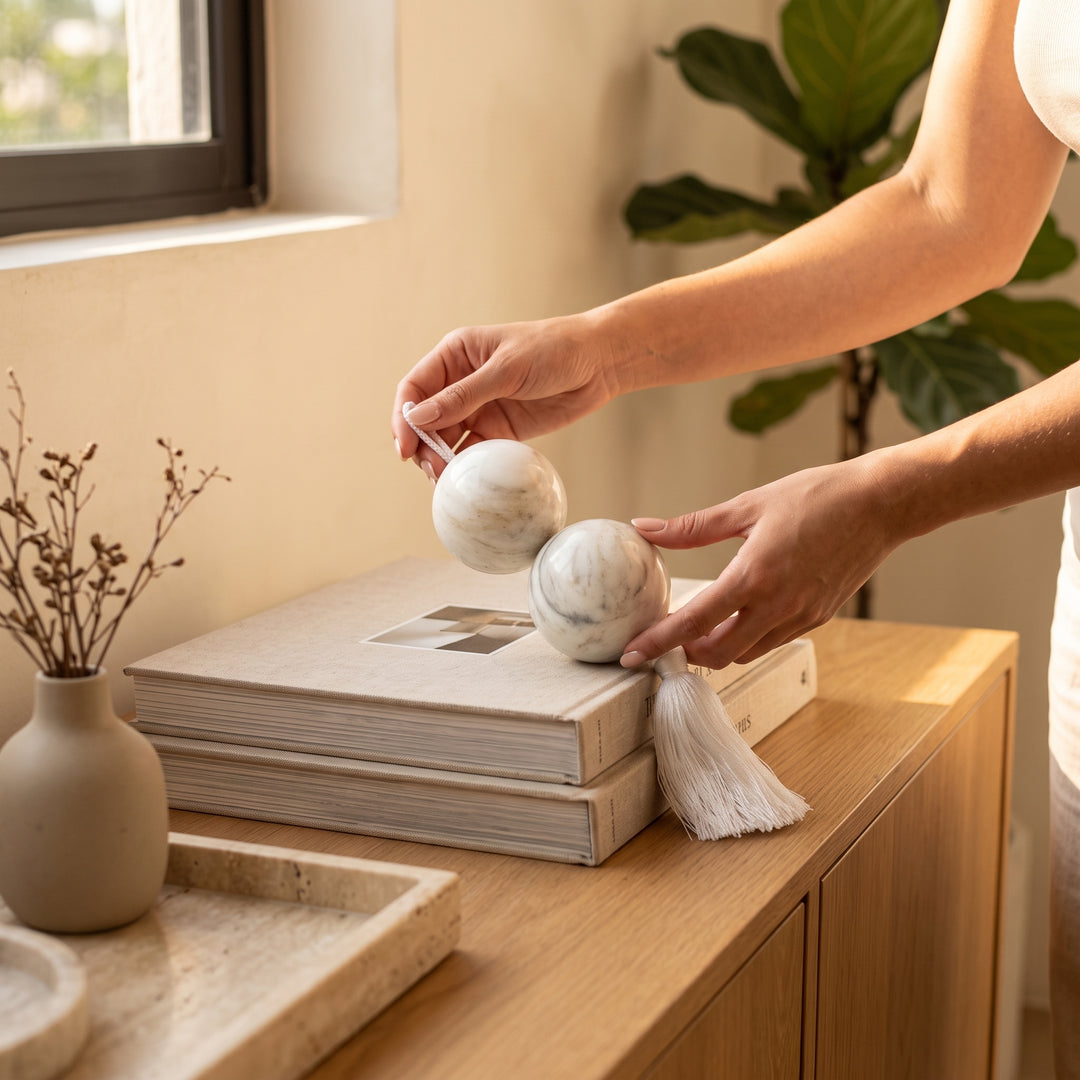 Manos colocando esferas bolas decoracion de mármol natural sólido con borla sobre libros en una credenza.