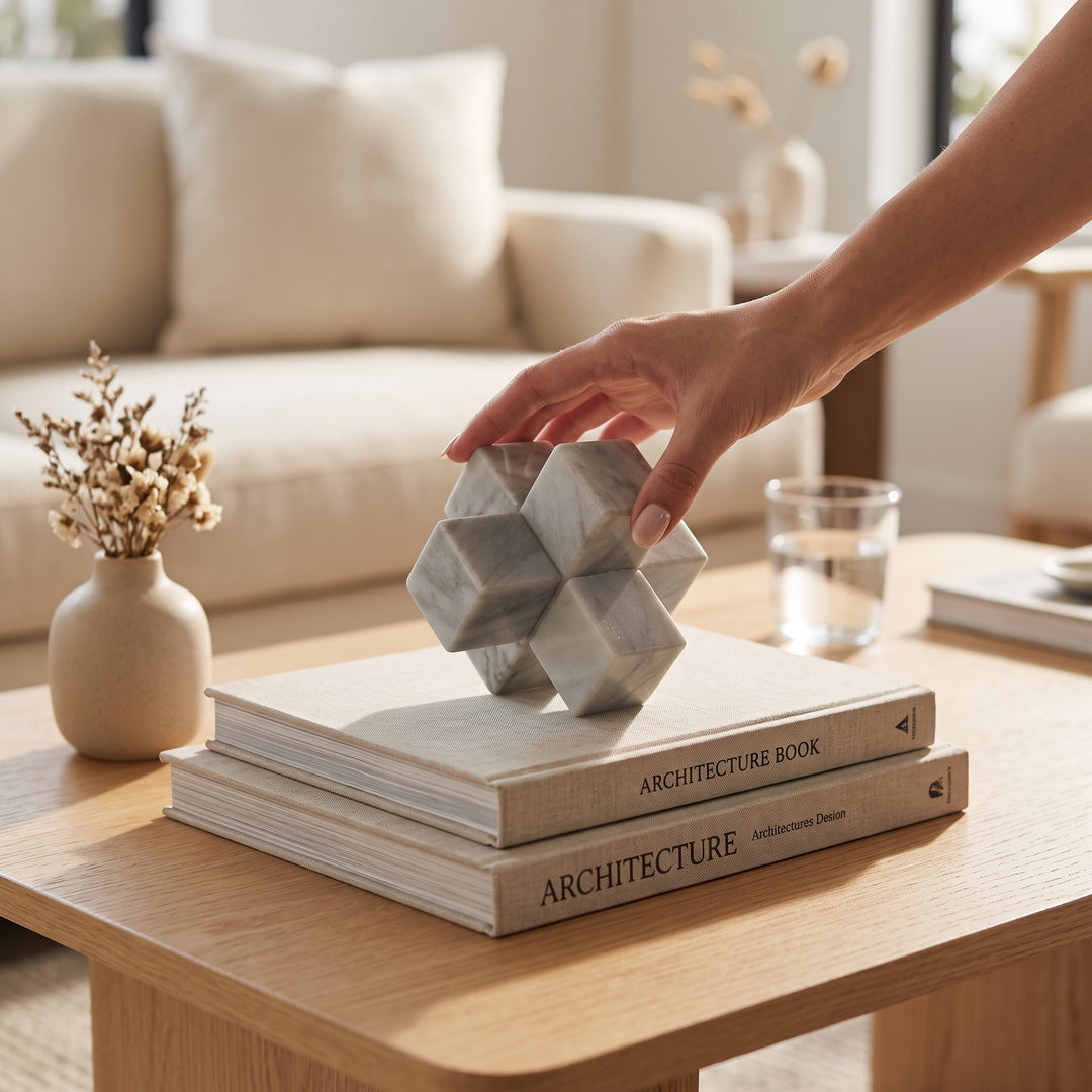 Mano colocando la escultura decorativa Matatena Nudo de mármol natural sobre libros en una mesa de centro.