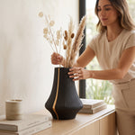 Cargar imagen en el visor de la Galería, Mujer colocando flores secas en el jarrón decorativo Halil sobre una mesa de madera.