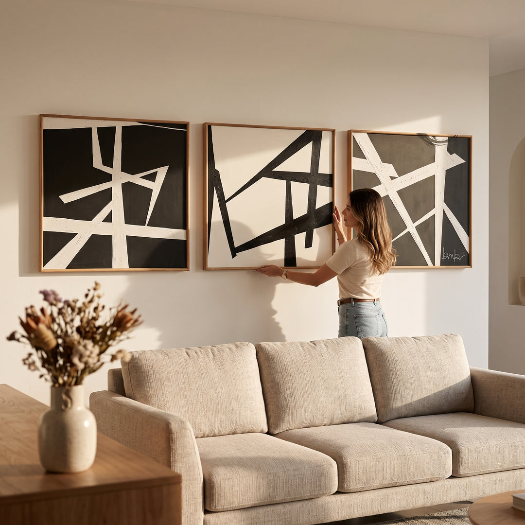 Mujer acomodando los Cuadros Decorativos Trazo Set 3 en Acrílico y Madera sobre un sofá en la sala.