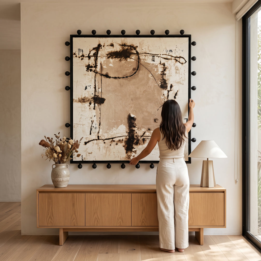 Mujer colocando el cuadro Moka texturizado técnica mixta con marco de madera 120x120 cm sobre aparador.