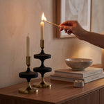 Cargar imagen en el visor de la Galería, Mano encendiendo una vela en los portavelas de metal decorativos Zia y Rohan sobre un mueble.