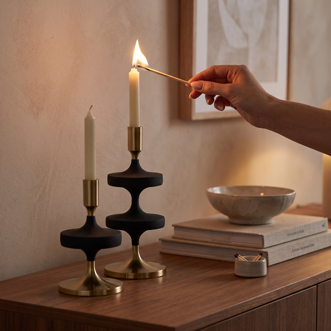 Mano encendiendo una vela en los portavelas de metal decorativos Zia y Rohan sobre un mueble.