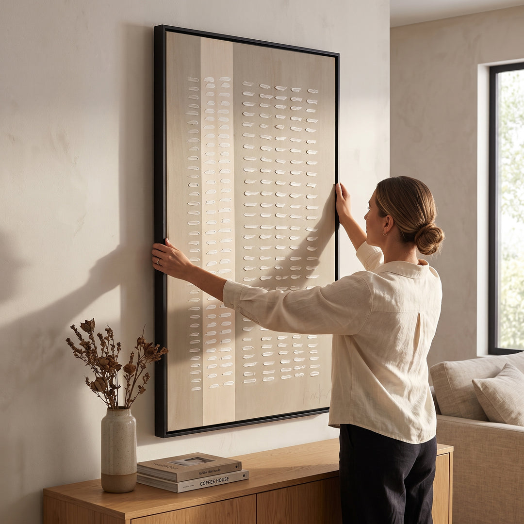 Mujer colgando el cuadro decorativo Sabi acrílico alto relieve de 90x150 cm en una moderna sala luminosa.
