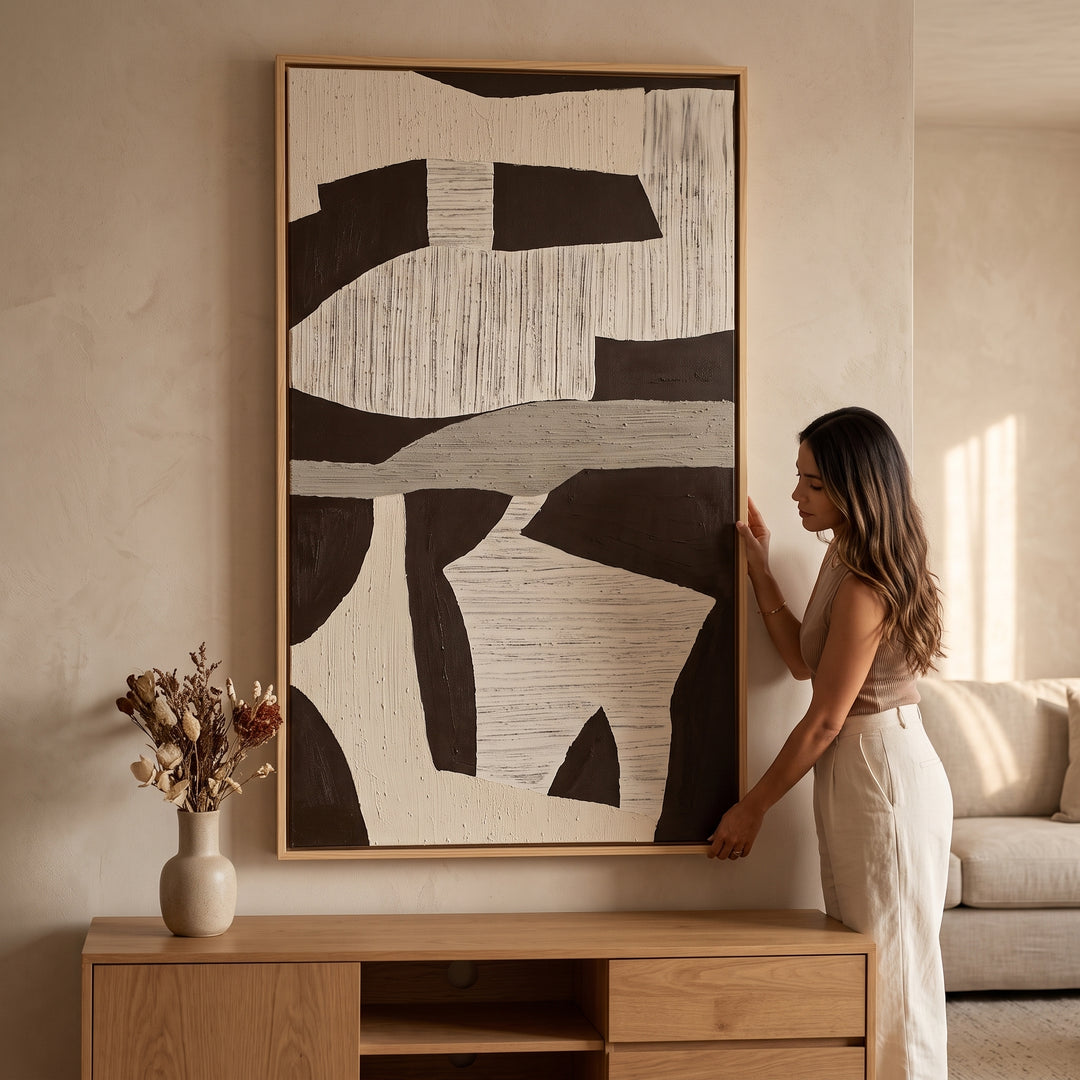 Mujer sosteniendo el cuadro Nómadas de arte abstracto en alto relieve con marco de madera de pino en una sala.