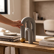 Accesorio decorativo Ramin de arcos grises y esfera dorada sobre una mesa de madera con libros.