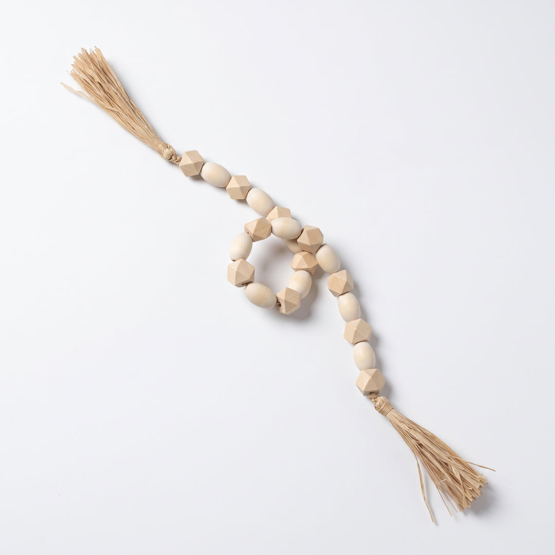 Guirnalda de cuentas decorativas Mala Tashi de MDF 77cm con borlas sobre fondo blanco.