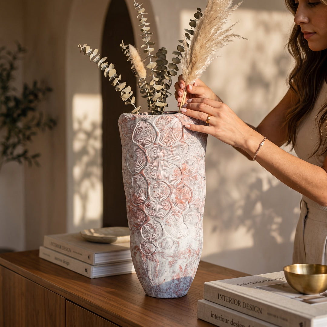Mujer decorando con flores secas el jarrón Hiro chico de cerámica texturizada sobre un mueble de madera.