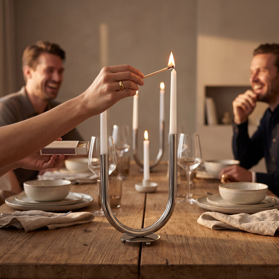 Mano encendiendo el candelabro portavelas en forma de U decorativo para comedor 25x35cm en la mesa.