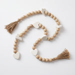 Cargar imagen en el visor de la Galería, Guirnalda de cuentas de corazón decorativas de madera y mármol con borlas de yute sobre fondo blanco.