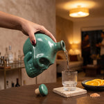Cargar imagen en el visor de la Galería, Mano sirviendo mezcal desde un tequilero calavera cerámica stoneware verde en un vaso de vidrio.
