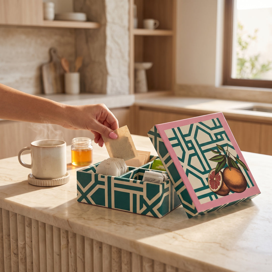 Mano sacando un sobre de la caja para té 19x19 cm con 4 divisiones junto a una taza caliente.