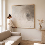 Mujer colgando el cuadro decorativo abstracto Áurea de 1.20x1.20cm en el muro de una sala moderna.