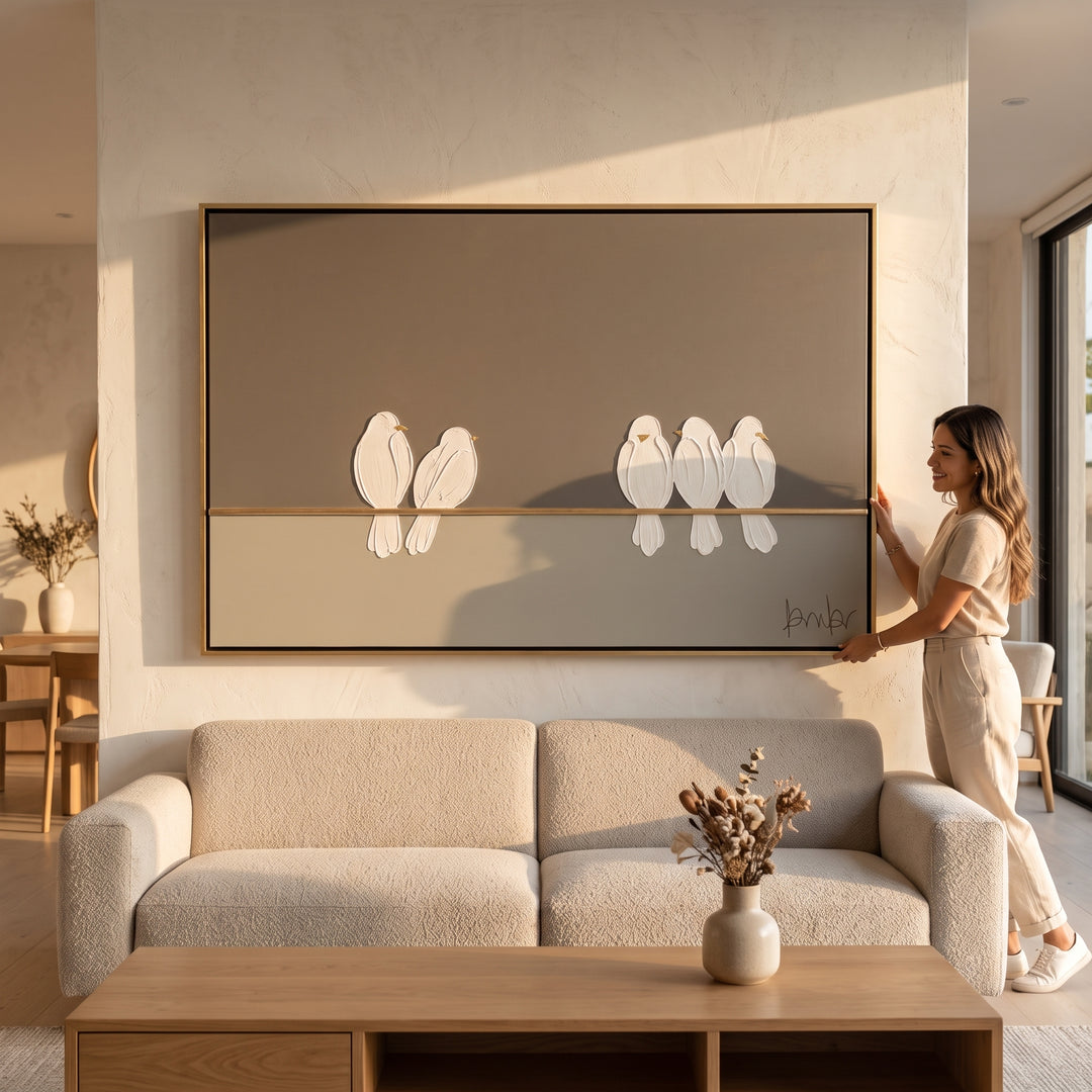 Mujer sosteniendo el Cuadro Quietud decorativo grande de aves sobre el sofá de una sala moderna.