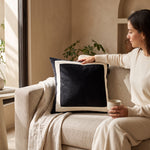 Cargar imagen en el visor de la Galería, Cojín Decorativo Maison Negro 50x50 cm con borde beige sobre un sofá junto a una mujer.