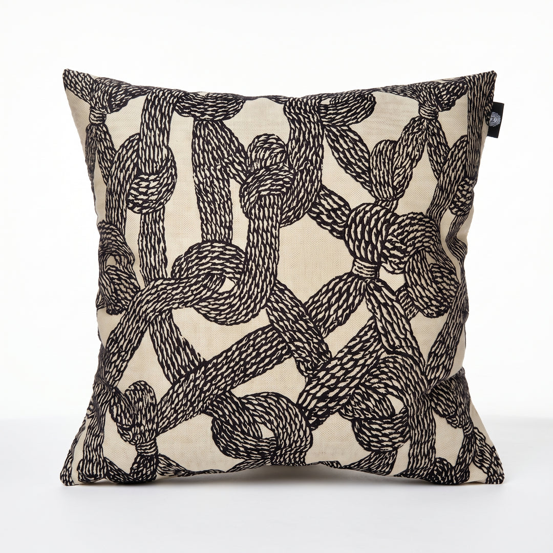 Cojín decorativo Cleopatra 50x50 cm con diseño de nudos de cuerdas negras sobre fondo beige.