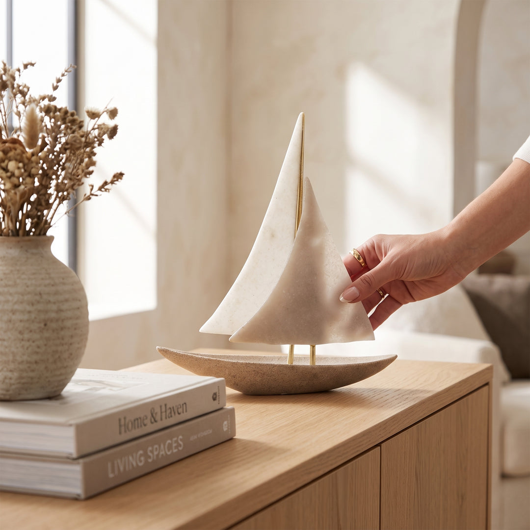 Figura decorativa de poliresina Barco Greda sobre un mueble de madera junto a libros y un florero.
