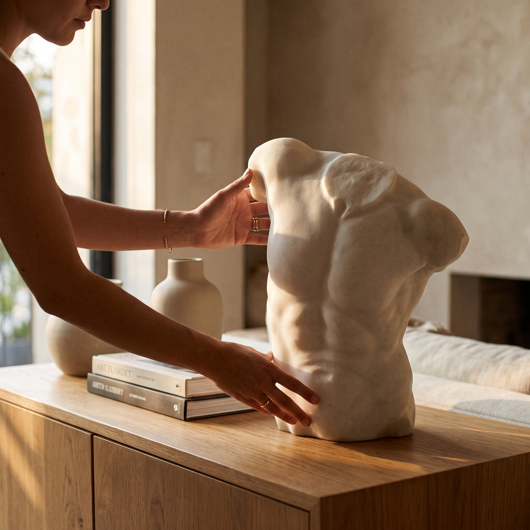 Manos colocando la figura Belia decorativa de poliresina sobre un mueble de madera junto a libros.