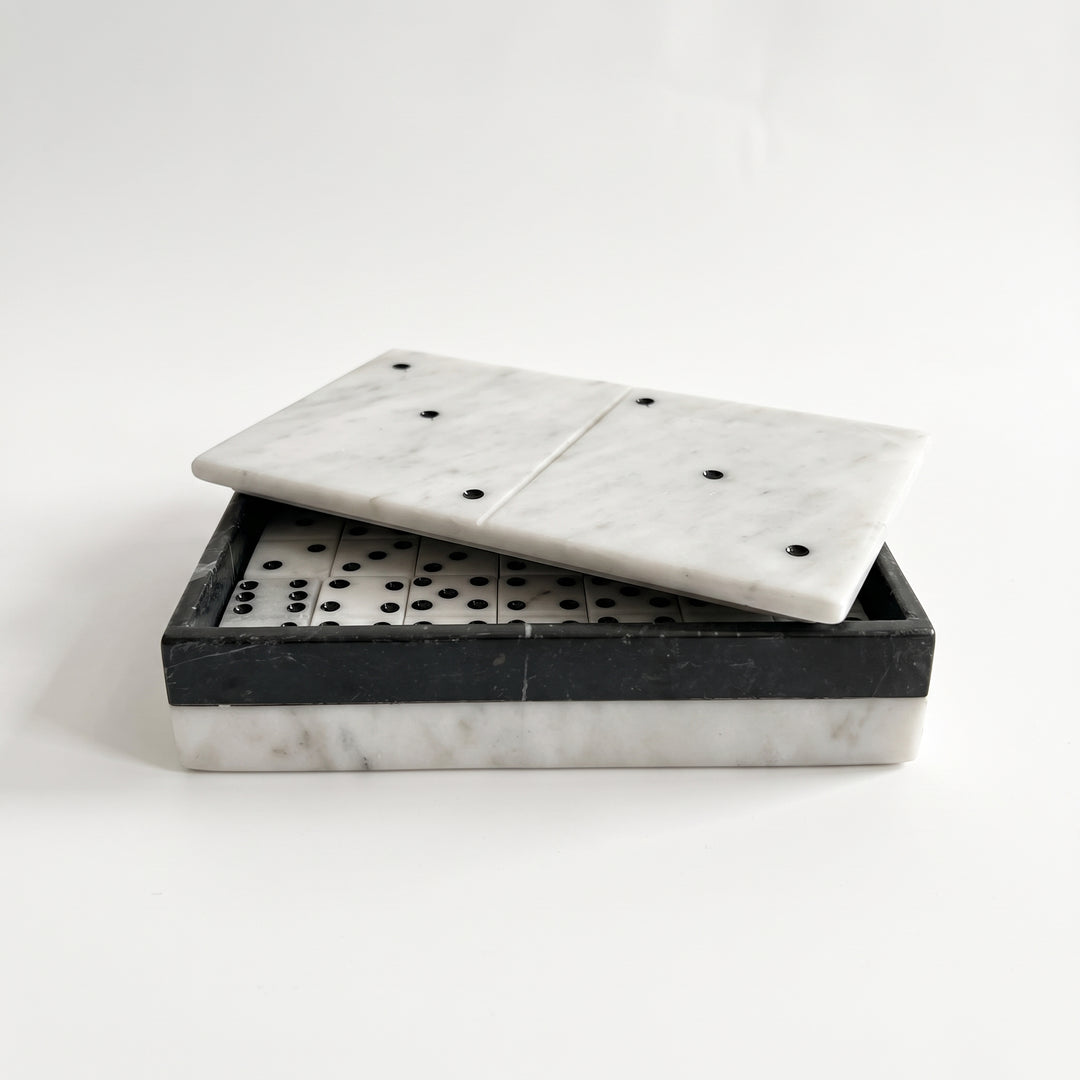 Caja de dominó bicolor de mármol blanco y negro entreabierta con fichas de juego en su interior.