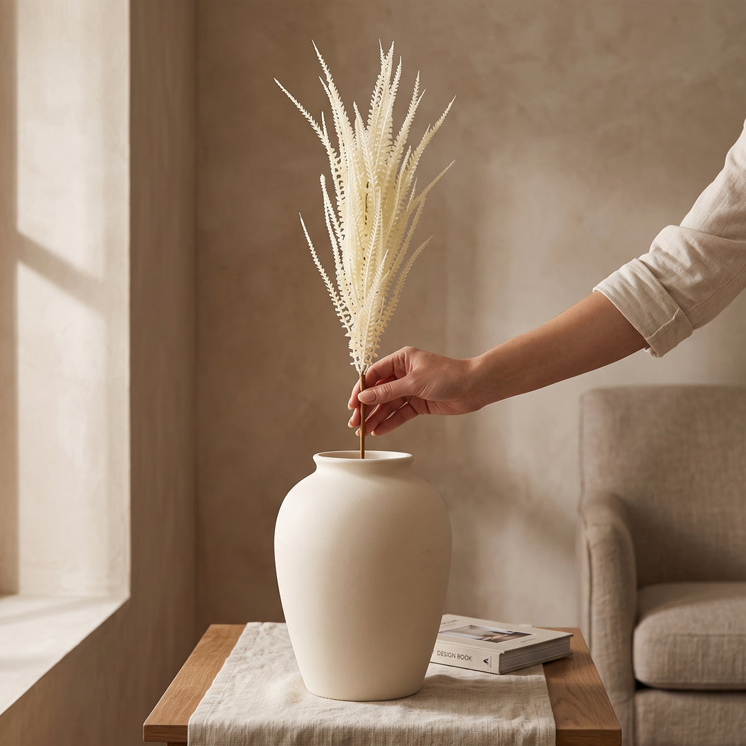 Mano colocando la vara sorgo decorativa para follaje de interior 106 en un jarrón de cerámica.