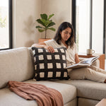 Cargar imagen en el visor de la Galería, Cojín decorativo Marmara Black en un sillón junto a una mujer leyendo en su sala.