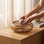 Cargar imagen en el visor de la Galería, Manos colocando una esfera en la base Liminal de cristal redonda de 25 cm para decoración sobre un mueble de madera.