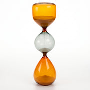 Reloj de arena decorativo de cristal de 35 cm con tres secciones en tonos ámbar y gris sobre fondo blanco.