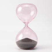 Reloj de Arena Marea de Cristal Rosa Decorativo 27 cm con arena oscura sobre fondo blanco.