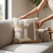 Cojín decorativo Silen beige 50 x 50 con diseño geométrico colocado sobre un sillón gris de sala.