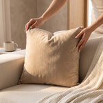Cargar imagen en el visor de la Galería, Manos colocando el cojín decorativo Luxemburgo beige 50x50 cm sobre un sillón con manta.