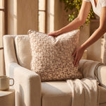 Cargar imagen en el visor de la Galería, Manos acomodando el cojín Breda Beige con textura sobre un sillón beige iluminado por el sol.