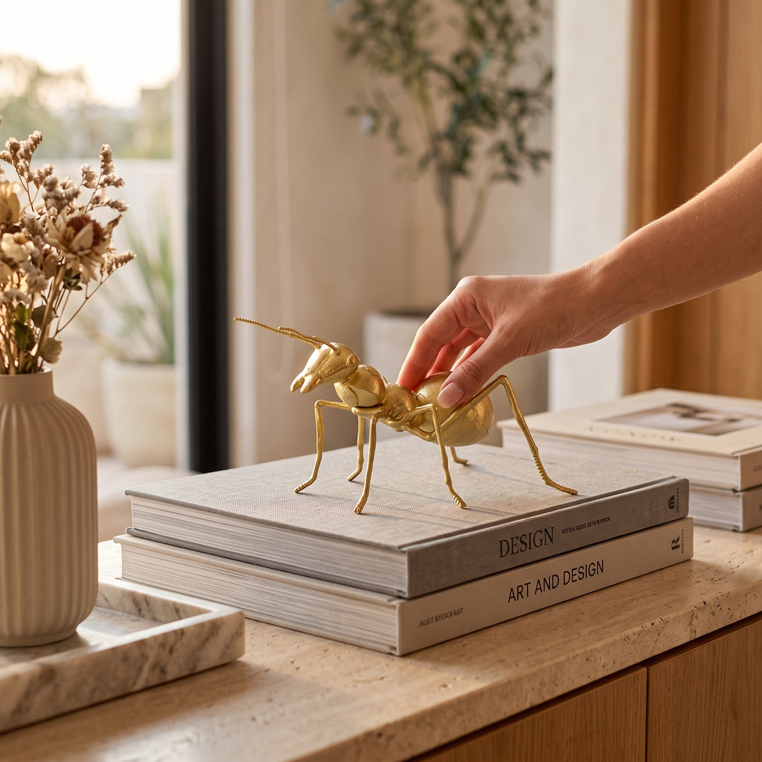 Figura decorativa Hormiga Ant Gold de resina dorado mate sobre libros de diseño en una sala.