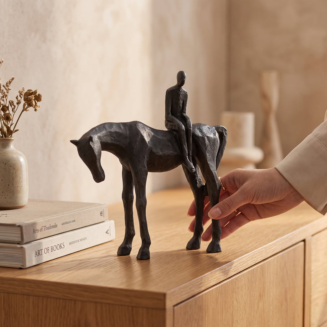 Escultura caballo y hombre decorativa de resina sobre una credenza de madera junto a libros.