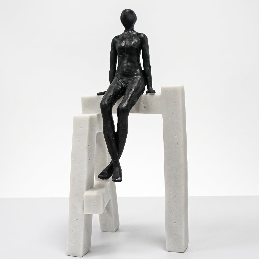 Escultura Hombre Sentado en Base I de Resina negra sobre estructura geométrica blanca.