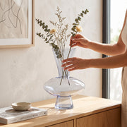 Jarrón Elba de cristal azul nube decorativo con ramas secas sobre un mueble de madera.