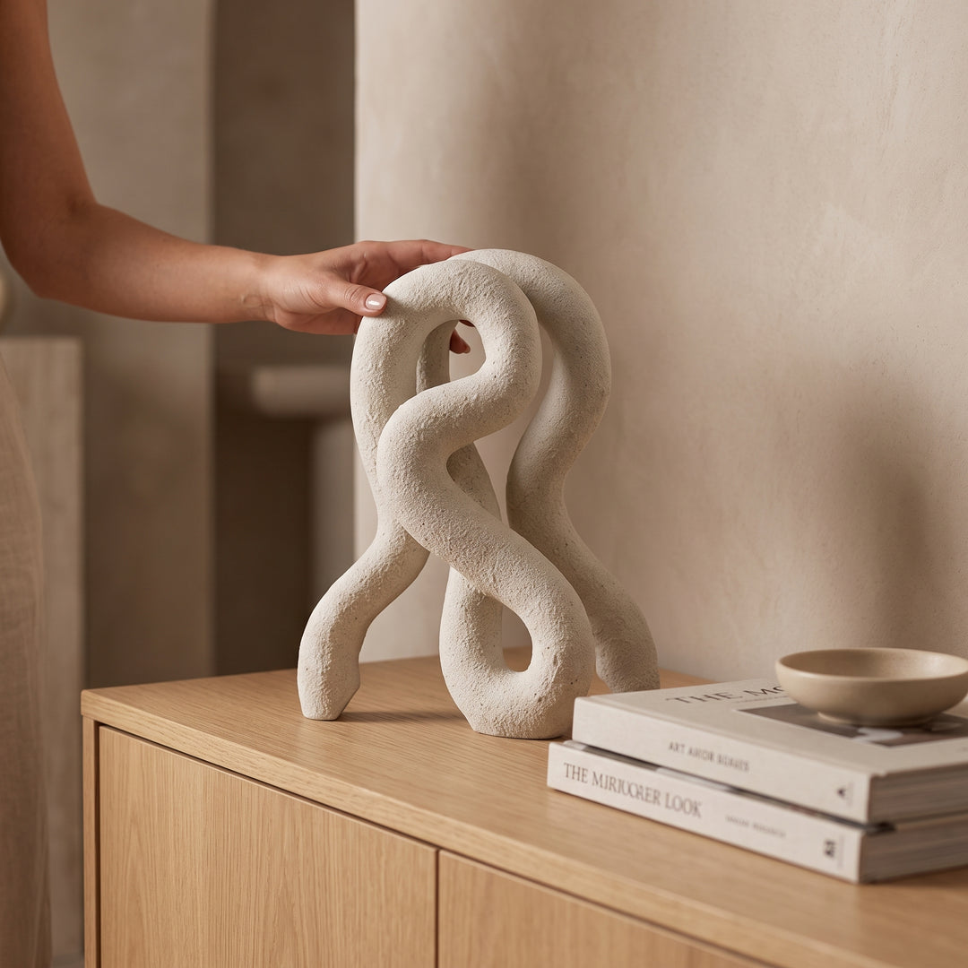 Accesorio decorativo Nerel de poliresina blanca 36 cm sobre mueble de madera junto a libros.