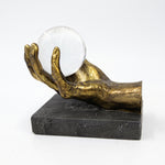 Cargar imagen en el visor de la Galería, Figura Saria escultura decorativa de mano dorada con esfera de cristal sobre base oscura.
