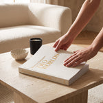 Cargar imagen en el visor de la Galería, Libro decorativo 2 mundos textil beige colocado sobre una mesa de centro junto a una vela y un cuenco.