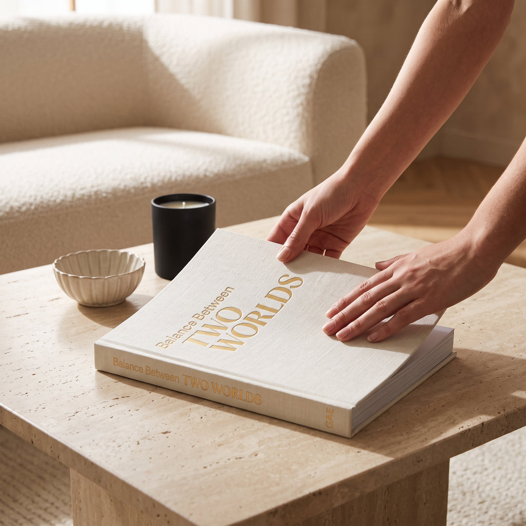 Libro decorativo 2 mundos textil beige colocado sobre una mesa de centro junto a una vela y un cuenco.