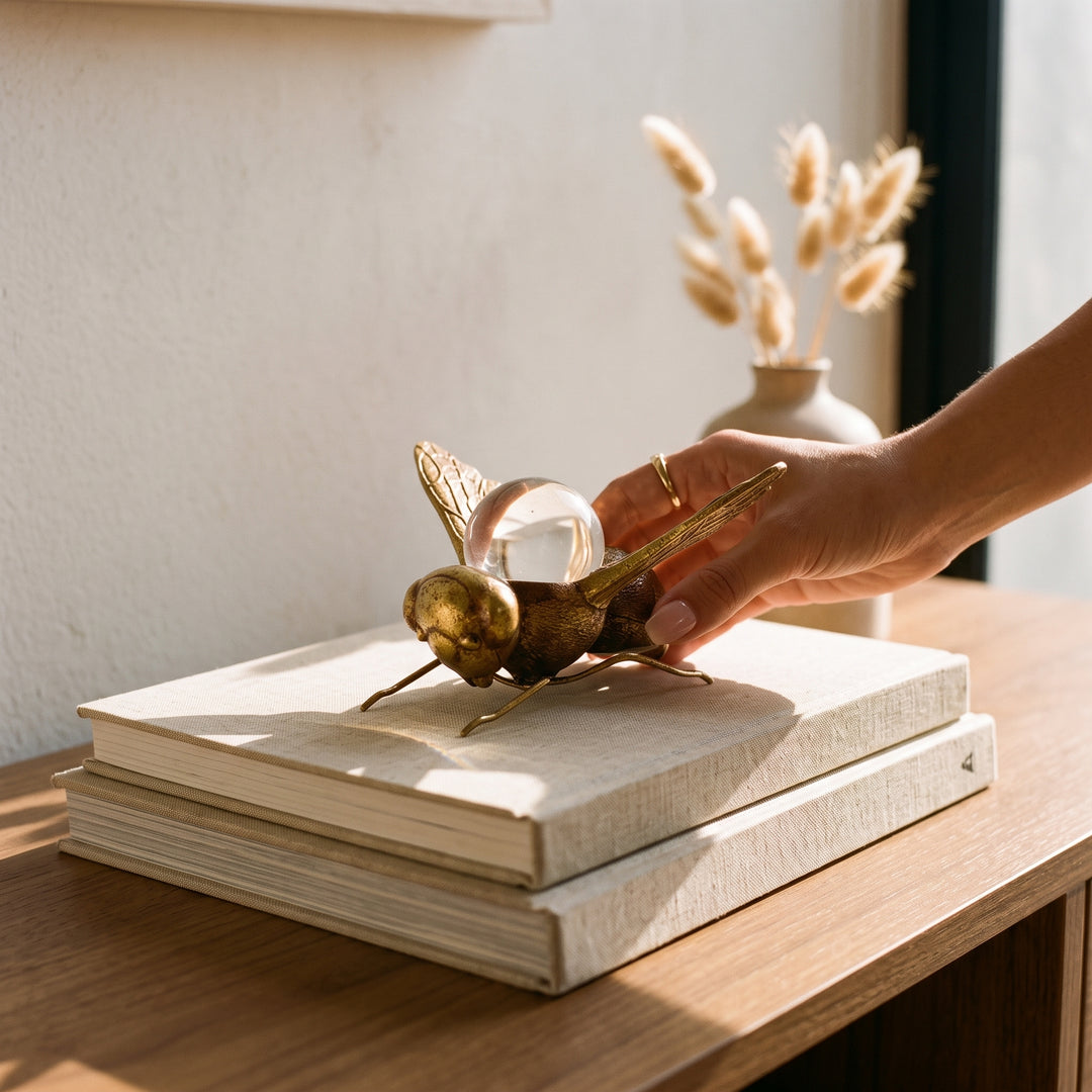 Mano tocando la figura decorativa de abeja Maren en metal y cristal sobre unos libros.