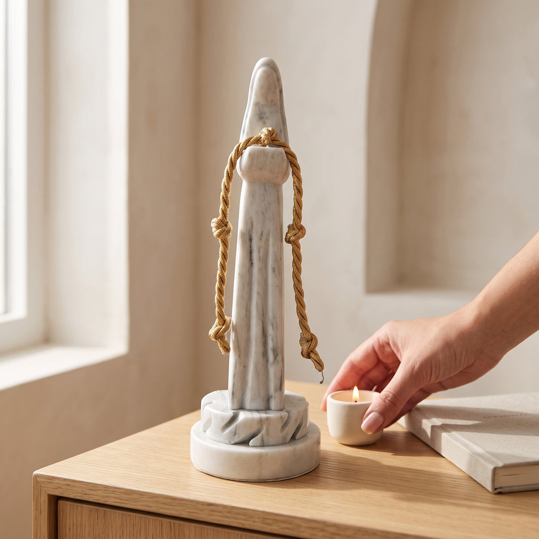Virgen Desatanudos de mármol blanco con cinta dorada en mesa de madera junto a una vela encendida.