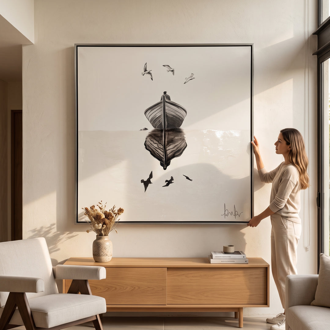 Mujer colgando el Cuadro Altamar en lienzo de 140 x 140 cm con marco hoja de plata en una sala moderna.